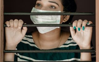 Woman looking outside between window bars with mask