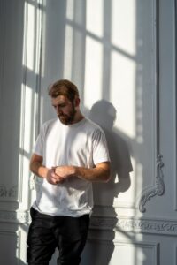 Man leaning against wall looking down wringing hands