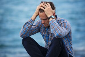 Man sitting next to water holding his head