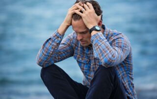 Man sitting next to water holding his head