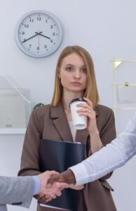 Woman in office with coffee cup and two people shaking hands