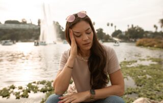 Woman sitting next to water holding her head