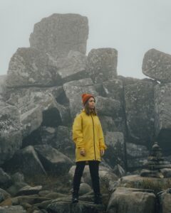 Woman standing on rocks in rain jacket and hat