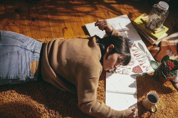 woman laying on floor drawing in journal