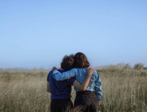 Two people in a field with arms around each other from the back