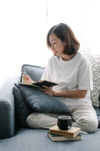 Woman sitting on couch with cup of tea and books writing in journal