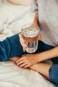 Woman sitting on bed holding glass of water