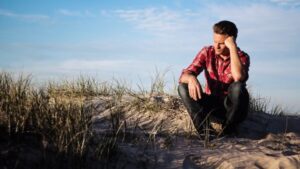 Man sitting on sand dune leaning on his fist