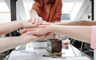 Woman reaching out hand to meet stacked hands with papers on dek