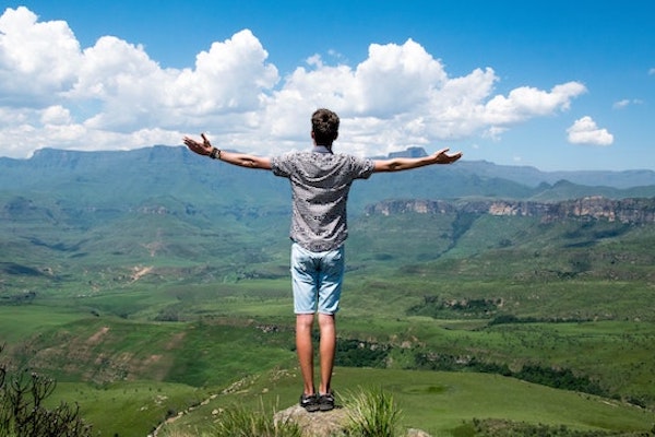 man standing look at view of mountains with arms stretched out wide
