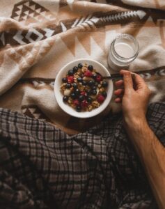Person holding spoon in bowl of cereal and berries