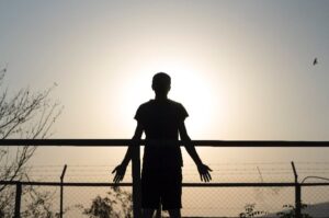 Silhouette of person looking over barbed wire fence at horizon