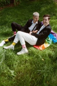two men sitting on rainbow flag in grass