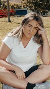 Woman sitting cross legged outside with two fingers on forehead
