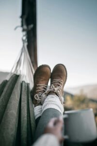 Legs of person in hiking shoes with mug in hammock