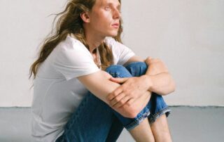 Man in jeans and white t-shirt sitting on floor with arms around legs