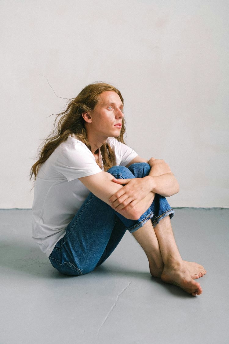 Man in jeans and white t-shirt sitting on floor with arms around legs