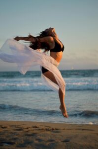 Dancer jumping over sandy shore of ocean