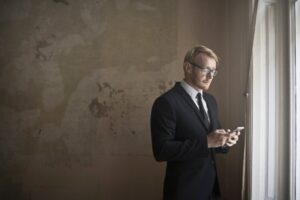 Man in suit and tie standing at a window looking at cell phone