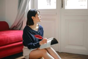 Woman sitting on floor with journal and feather pen looking out window