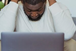 Man with hands on head furrowed brow in front of laptop